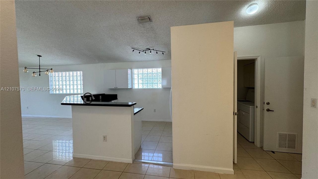 Kitchen featuring a raised breakfast bar with dark solid-surface countertops, white cabinetry, glass block windows, and ceramic tile flooring
