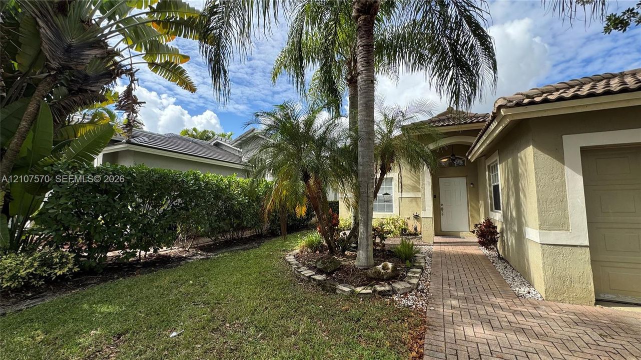 Exterior facade featuring a stucco finish, arched entryway, brick-paver walkway, tile roof, and mature palm landscaping
