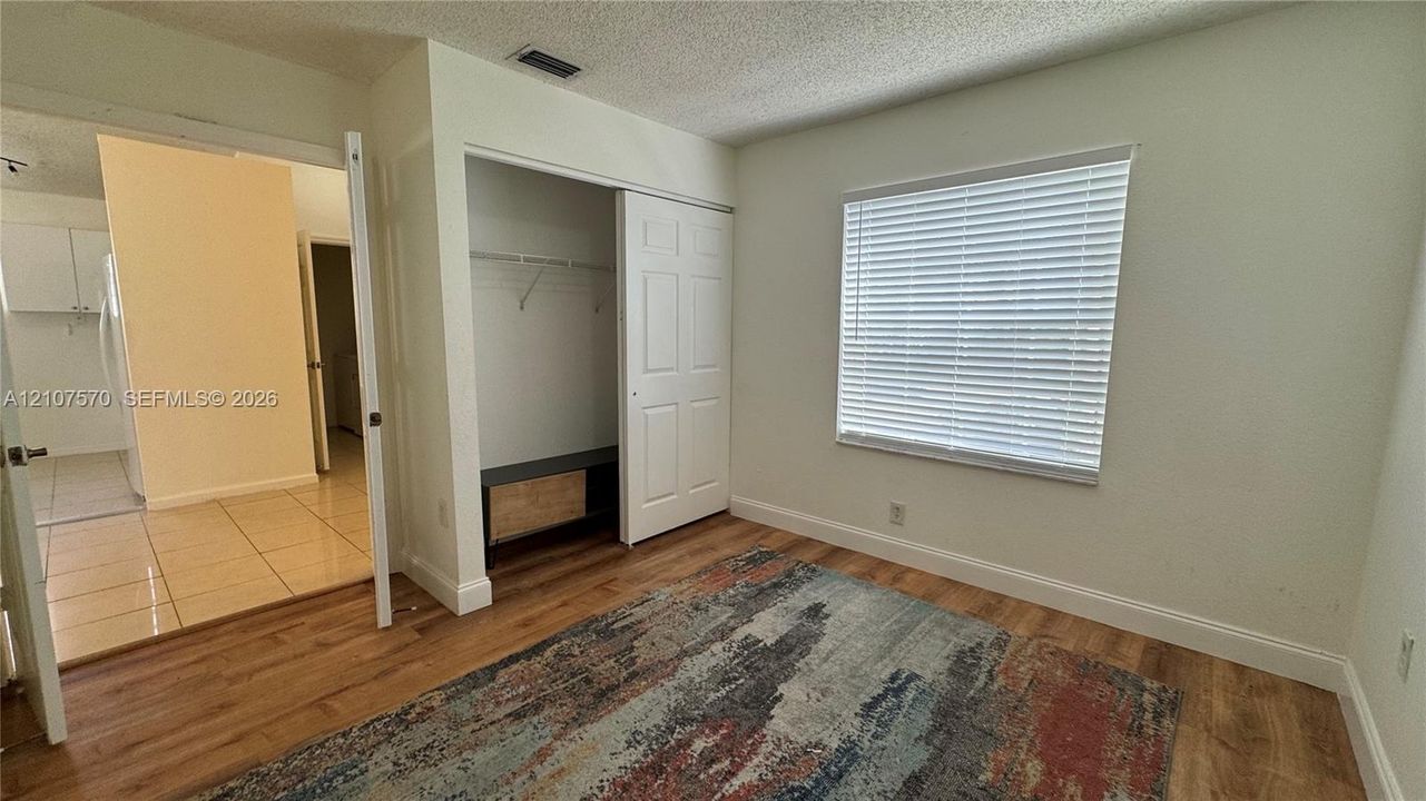 Wood-finish flooring, sliding door closet with built-in shelving, and window with installed horizontal blinds