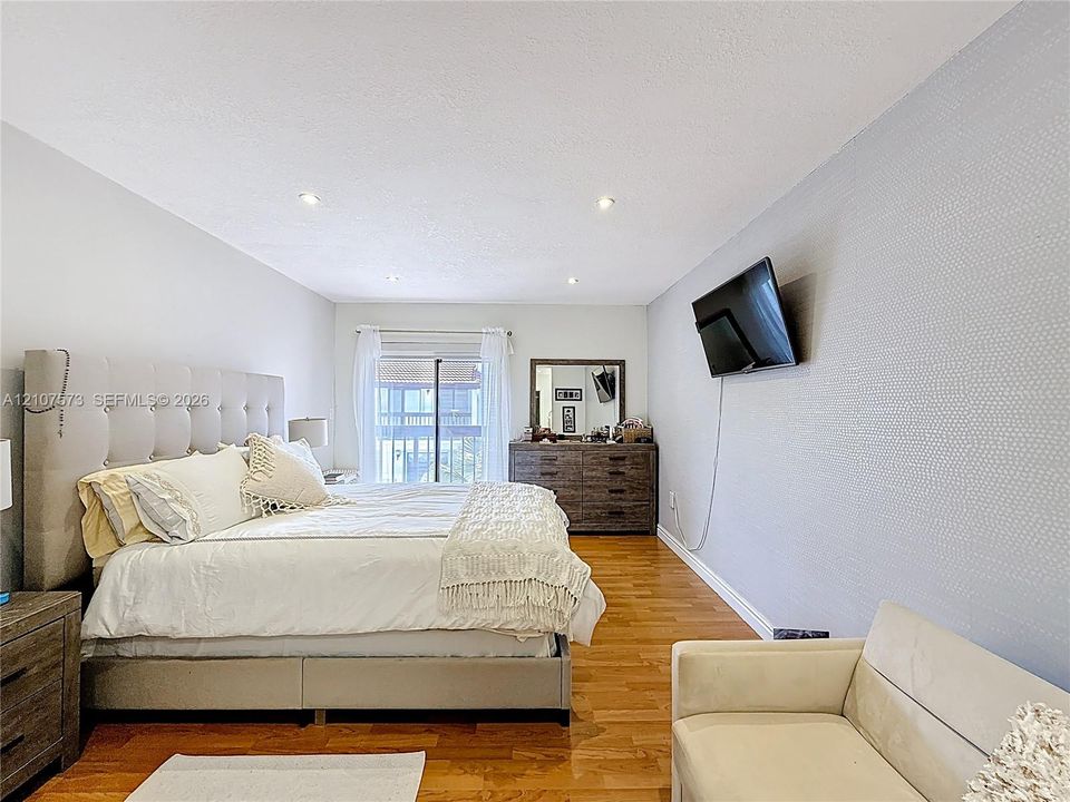 Interior space featuring wood-finish flooring, recessed lighting, and a textured accent wall with sliding glass door access to an exterior balcony