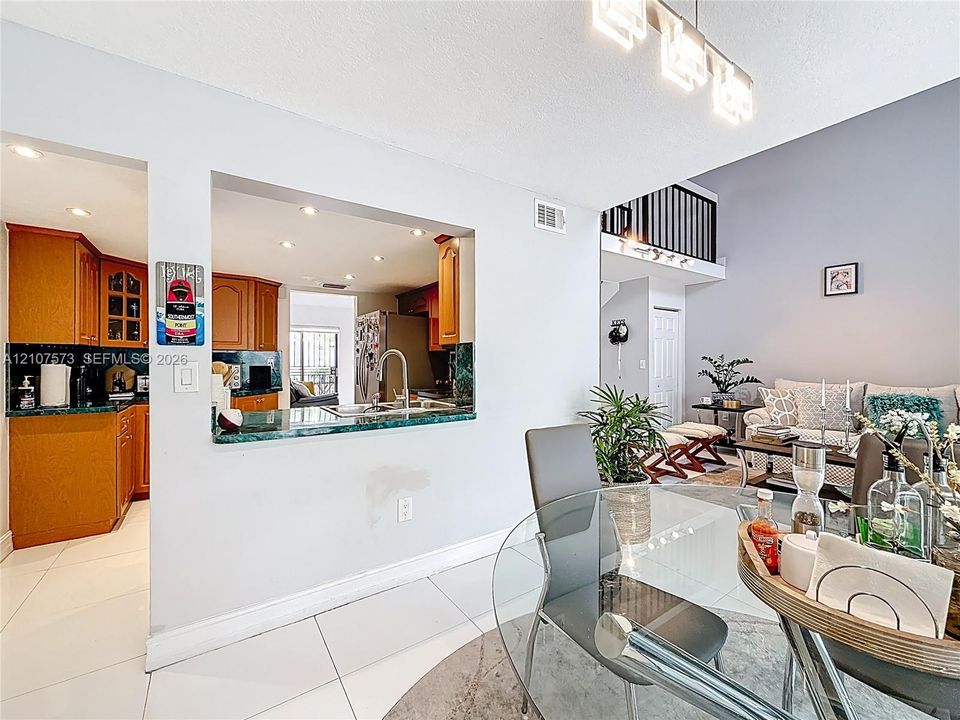 Kitchen features a pass-through window with a stone-surface countertop, cabinetry with glass-panel detailing, recessed lighting, and white tile flooring