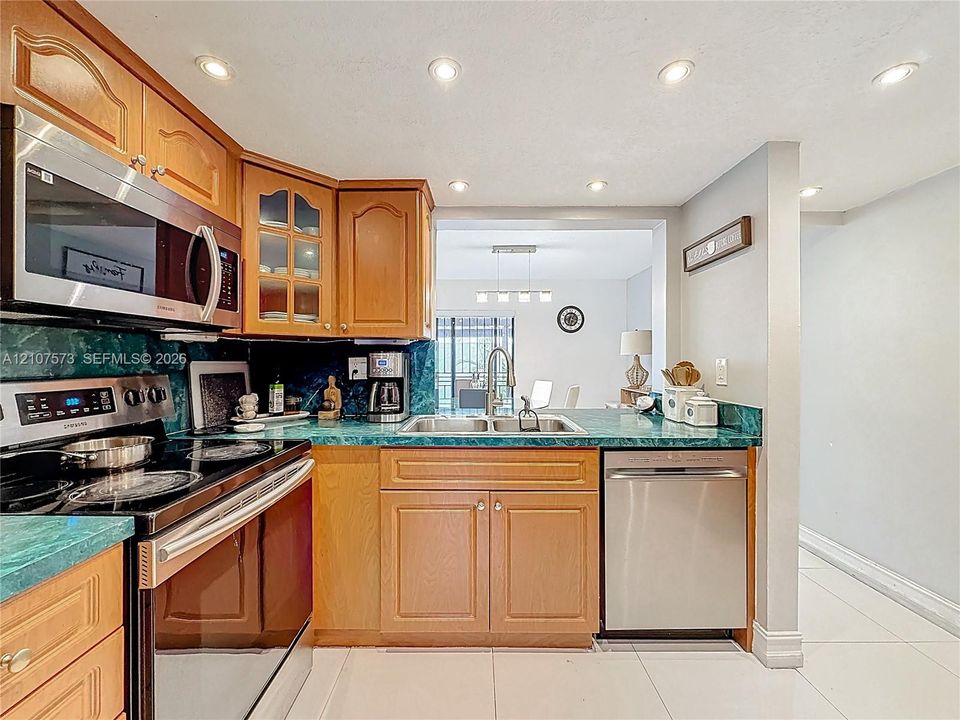 Kitchen featuring wood cabinetry with glass-front detailing, stainless steel microwave and dishwasher, solid-surface countertops, and recessed ceiling lighting