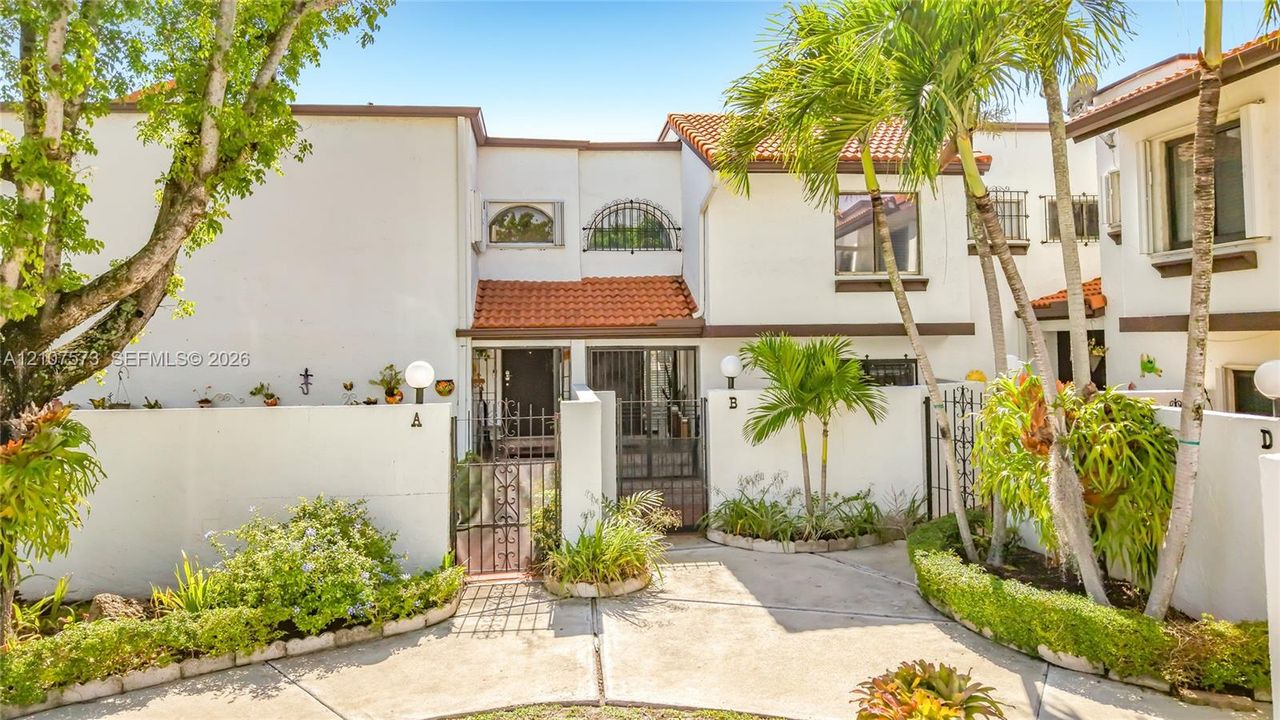 Stucco exterior featuring arched windows, tile roofing, decorative wrought-iron entry gates, and mature palm landscaping