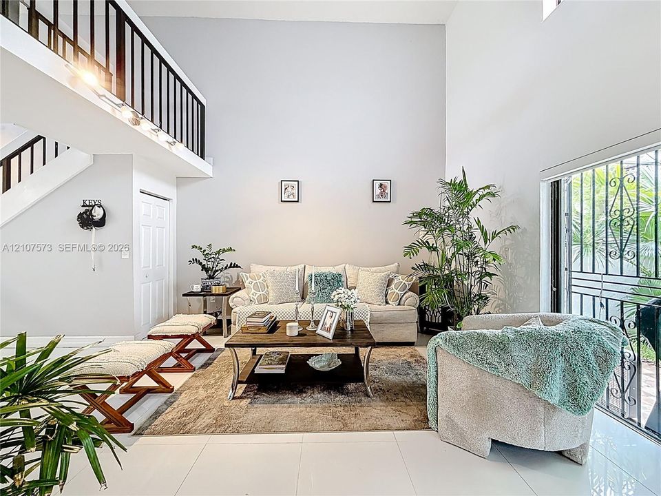 Living room featuring soaring double-height ceilings, ceramic tile flooring, and a mezzanine level with black balusters