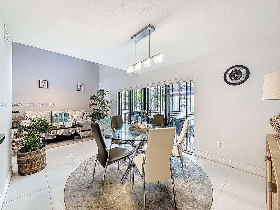 High-ceiling dining area featuring large-format tile flooring, a contemporary four-light linear pendant fixture, and sliding glass doors with metal security screening