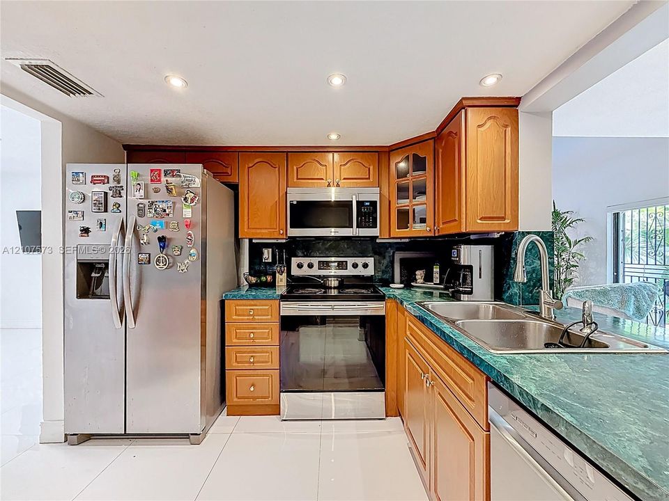 Kitchen featuring medium-tone wood cabinetry, green stone countertops, stainless steel appliances, and recessed lighting