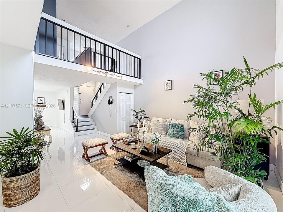 Double-height ceiling, polished tile flooring, and a metal-railed mezzanine overlooking the space, complemented by a central staircase with metal railings