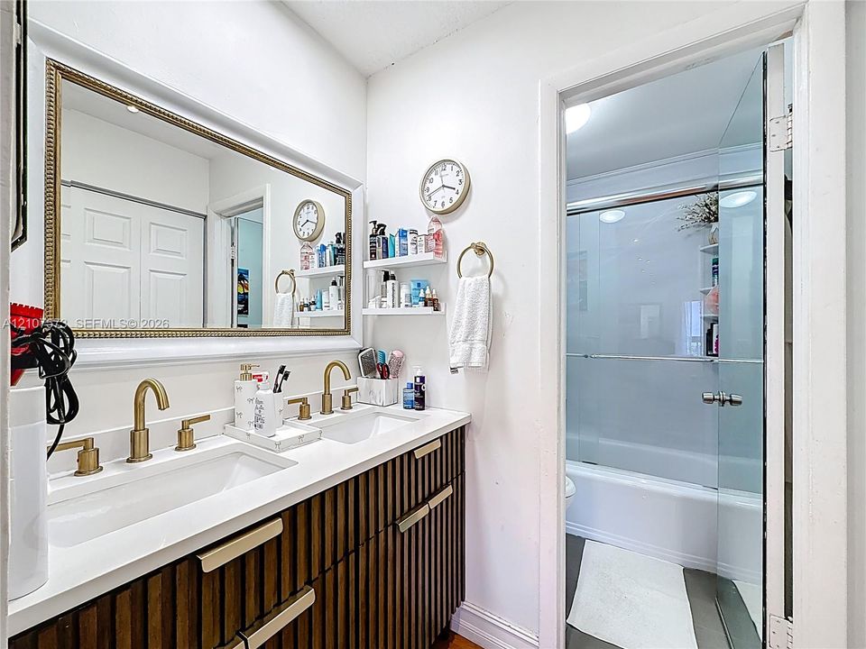 Double vanity featuring a white countertop, dual undermount sinks, brass-finish faucets, vertical-slat cabinetry with metallic hardware, and a framed wall mirror