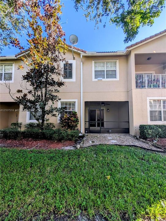 Stucco exterior featuring a screened-in lanai, stone-paver patio, second-story balcony with metal railing, and mature landscaping