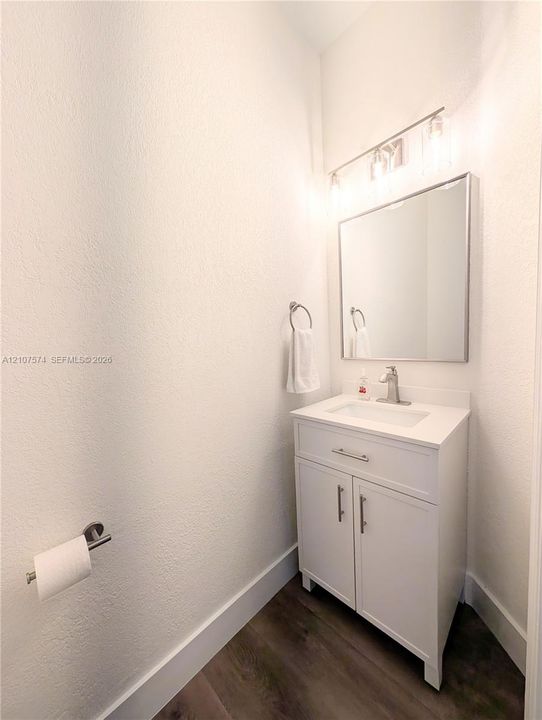 White vanity with a rectangular sink, stone-finish countertop, framed wall mirror, multi-light fixture, and wood-finish flooring