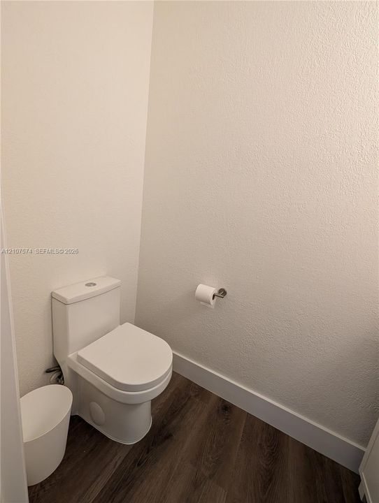 White dual-flush toilet featuring a concealed trapway, complemented by wood-finish flooring and a chrome toilet paper holder