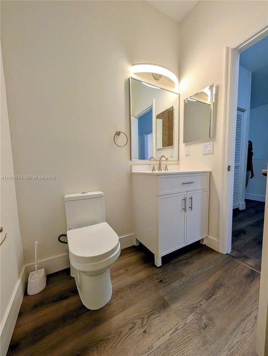 White vanity with integrated countertop, chrome faucet, rectangular mirror with arched light fixture, and wood-finish flooring