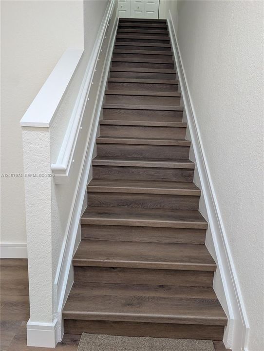 Staircase featuring wood-finish treads, white painted millwork, and a partial height pony wall