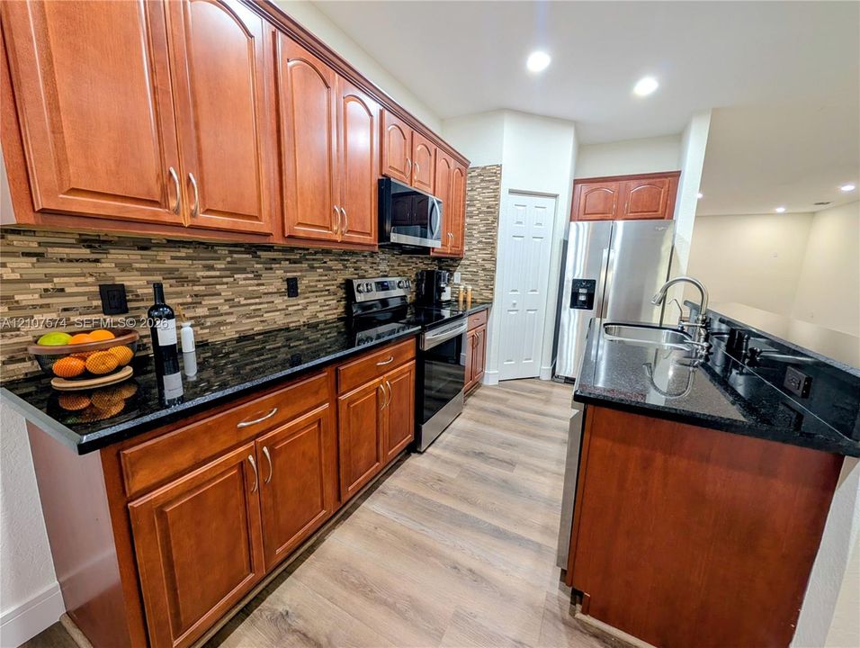 Kitchen featuring wood-finish cabinetry, dark stone-style countertops, a mosaic tile backsplash, stainless steel appliances, and wood-finish flooring