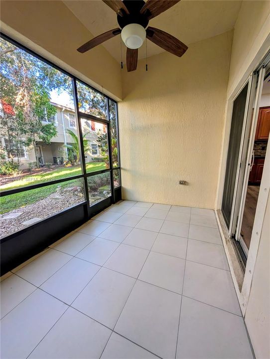Screened-in patio featuring tile flooring, a ceiling fan with light fixture, and floor-to-ceiling glass panel walls