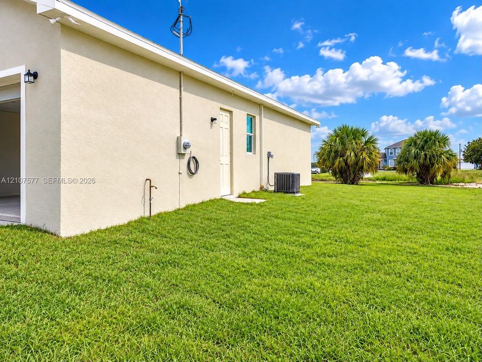 Stucco exterior with an expansive grass lawn, exterior wall-mounted lighting, and an outdoor water spigot