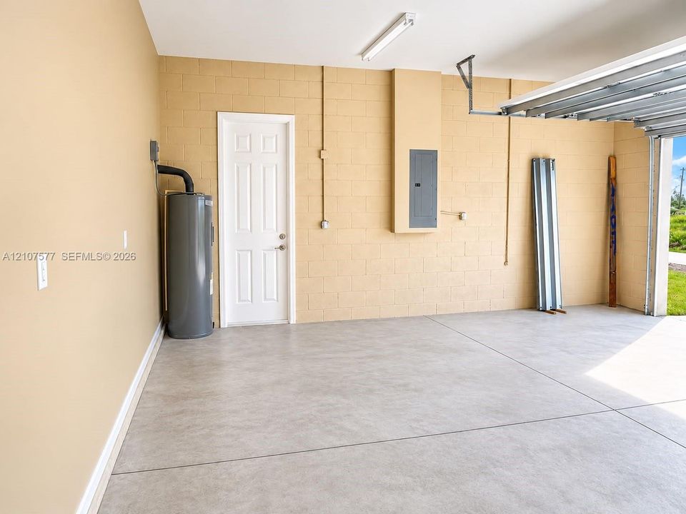 Garage interior featuring concrete masonry unit walls, a concrete floor, a six-panel door, a dedicated electrical panel, and a water heater