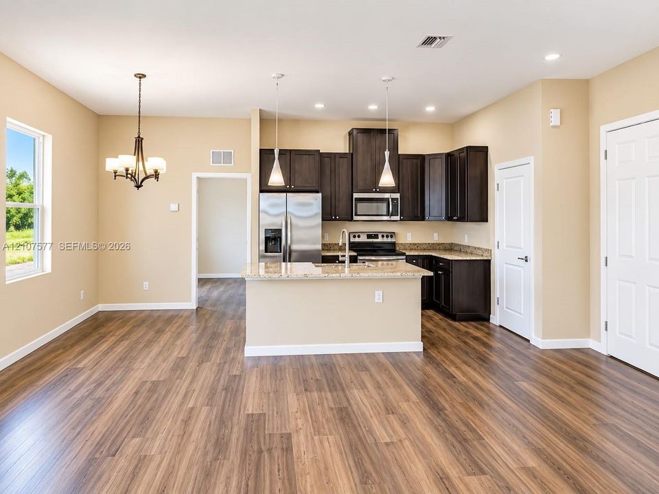 Kitchen featuring wood-finish flooring, dark cabinetry, stone-surface countertops, a center island with pendant lighting, and stainless steel appliances