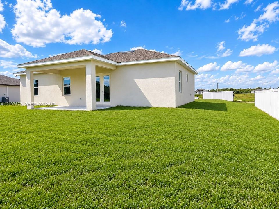 Stucco exterior featuring a covered patio, shingle roof, glass-paneled double doors, and a fenced backyard