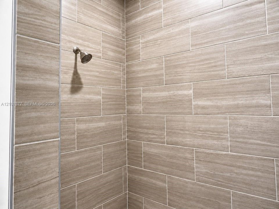 Walk-in shower enclosure featuring large-format neutral-tone tile and a wall-mounted shower head