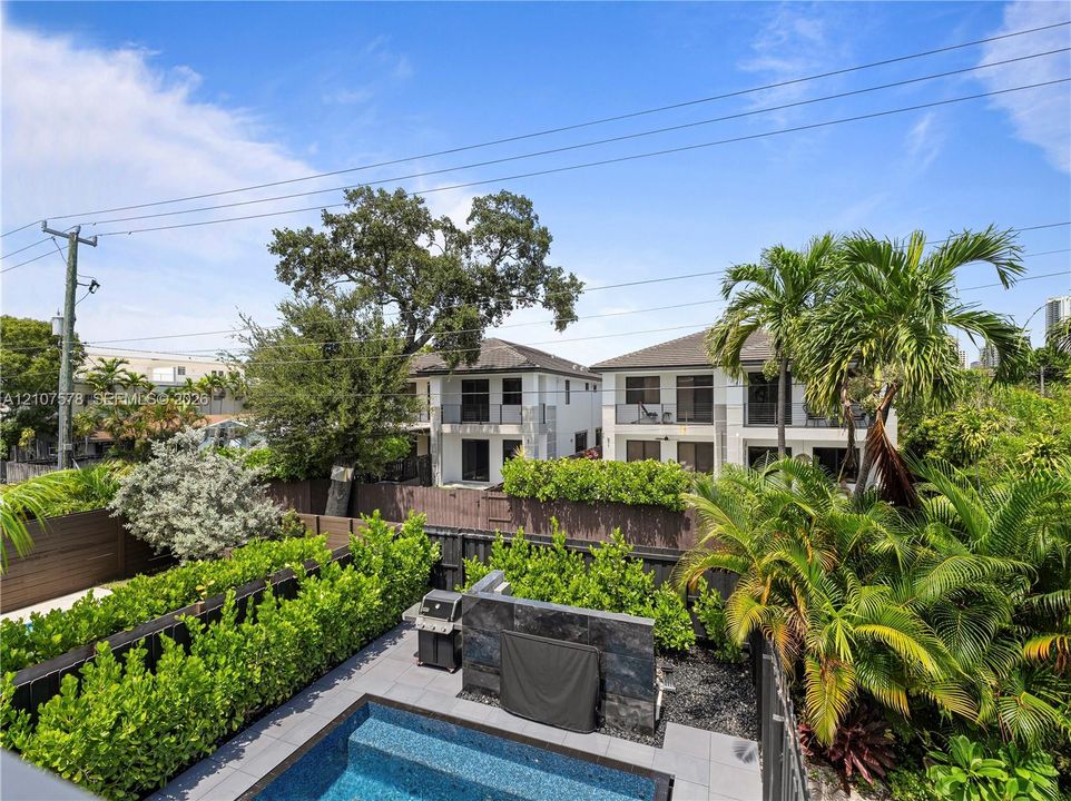Backyard featuring a custom pool, tiered stone-finish accent wall, slate-style patio decking, and perimeter privacy hedges