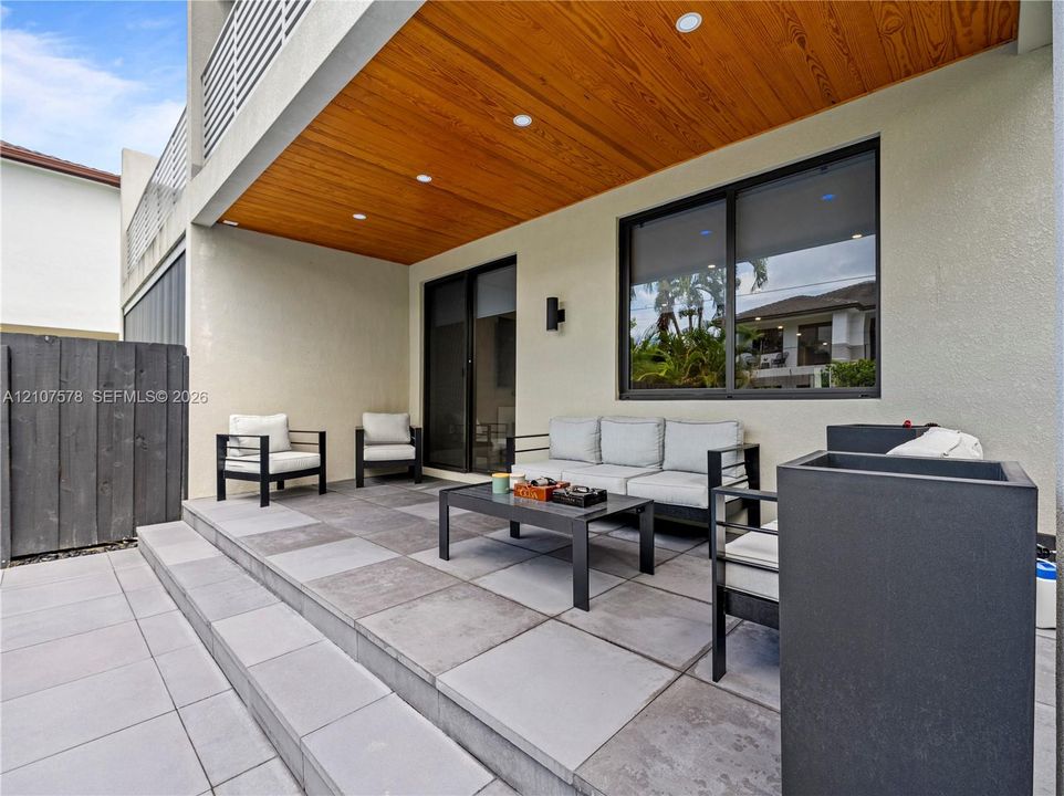 Covered patio featuring a wood-panel ceiling, recessed lighting, large-format tile flooring, and integrated black-framed windows and sliding glass doors
