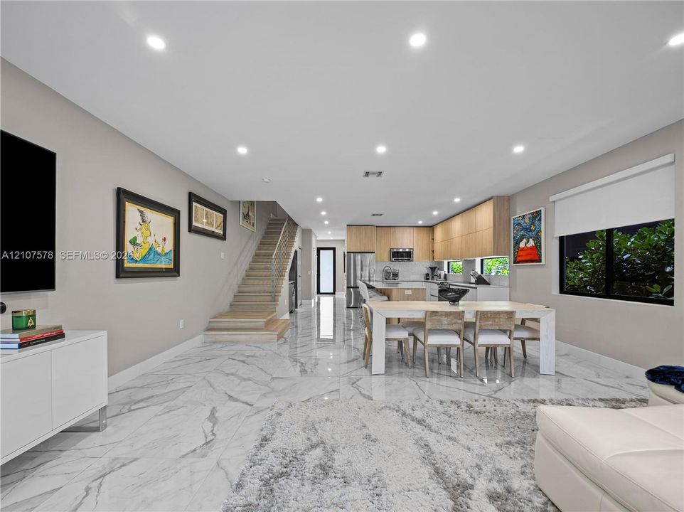 Large-format stone-finish tile flooring, recessed ceiling lighting, wood-finish flat-panel cabinetry, and staircase with metal cable railing