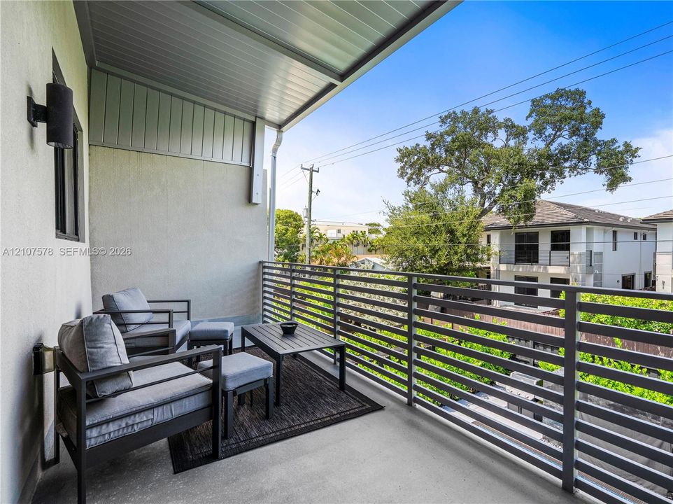 Covered balcony featuring concrete flooring, horizontal metal railing, and wall-mounted exterior lighting