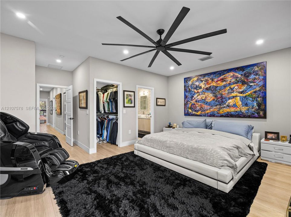 Light-toned wood-finish flooring, recessed lighting, multi-blade matte black ceiling fan, and walk-in closet with built-in storage