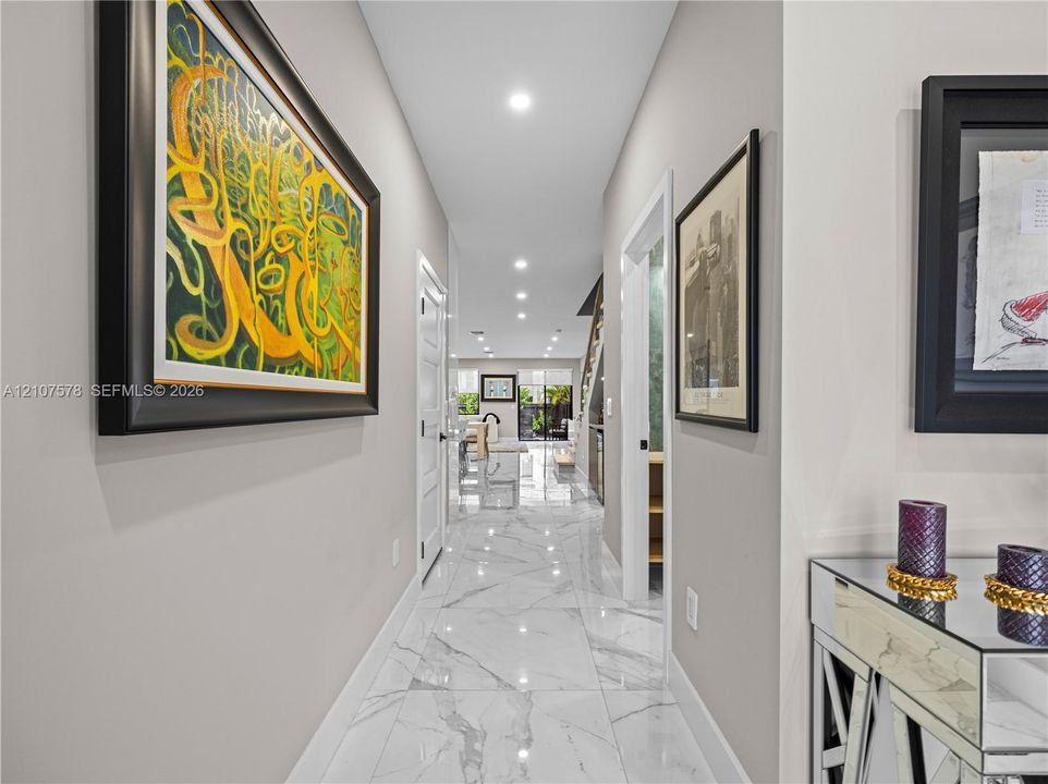 Neutral-toned interior hallway featuring large-format stone-finish tile flooring, recessed ceiling lighting, and multi-panel interior doors