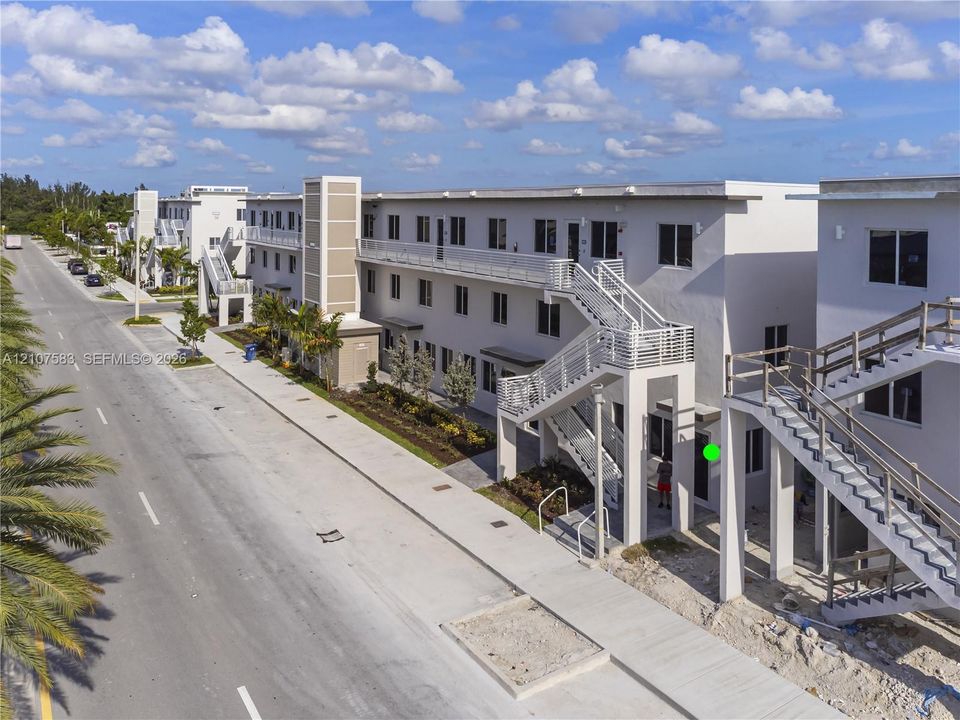 Multi-story exterior featuring light-toned stucco siding, metal staircases, exterior walkways with horizontal railings, and integrated wall-mounted lighting