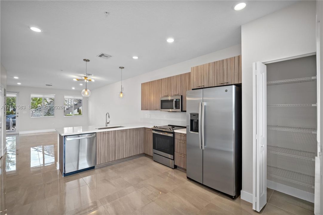 Kitchen featuring wood-finish cabinetry, stainless steel appliances, a peninsula with an integrated sink, polished tile flooring, and a walk-in pantry with built-in shelving
