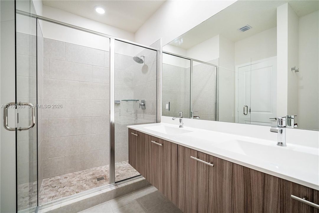 Floating vanity with wood-finish cabinetry, dual undermount sinks, quartz countertops, and a full-width mirror