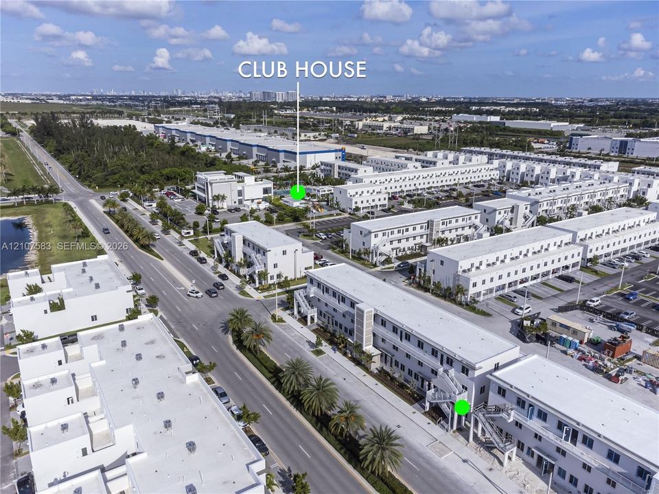 Aerial perspective of a multi-unit residential development featuring a dedicated clubhouse, paved parking areas, and mature palm landscaping