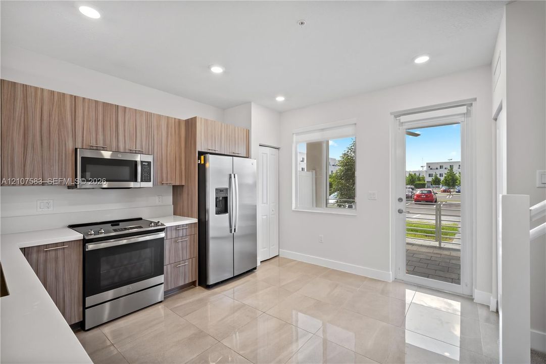 Kitchen featuring flat-panel wood-finish cabinetry, white countertops, stainless steel appliances, tile flooring, and a glass-panel door