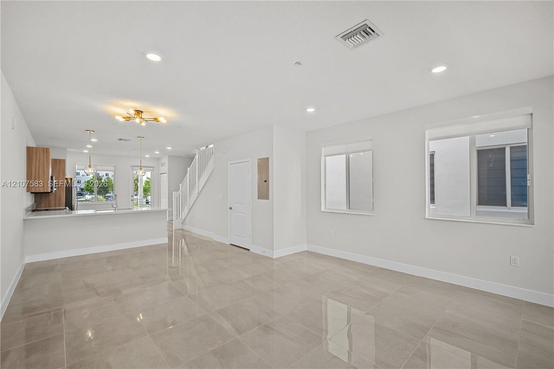 Large-format tile flooring, recessed ceiling lighting, kitchen featuring wood-finish cabinetry, breakfast bar, and staircase with wooden handrail