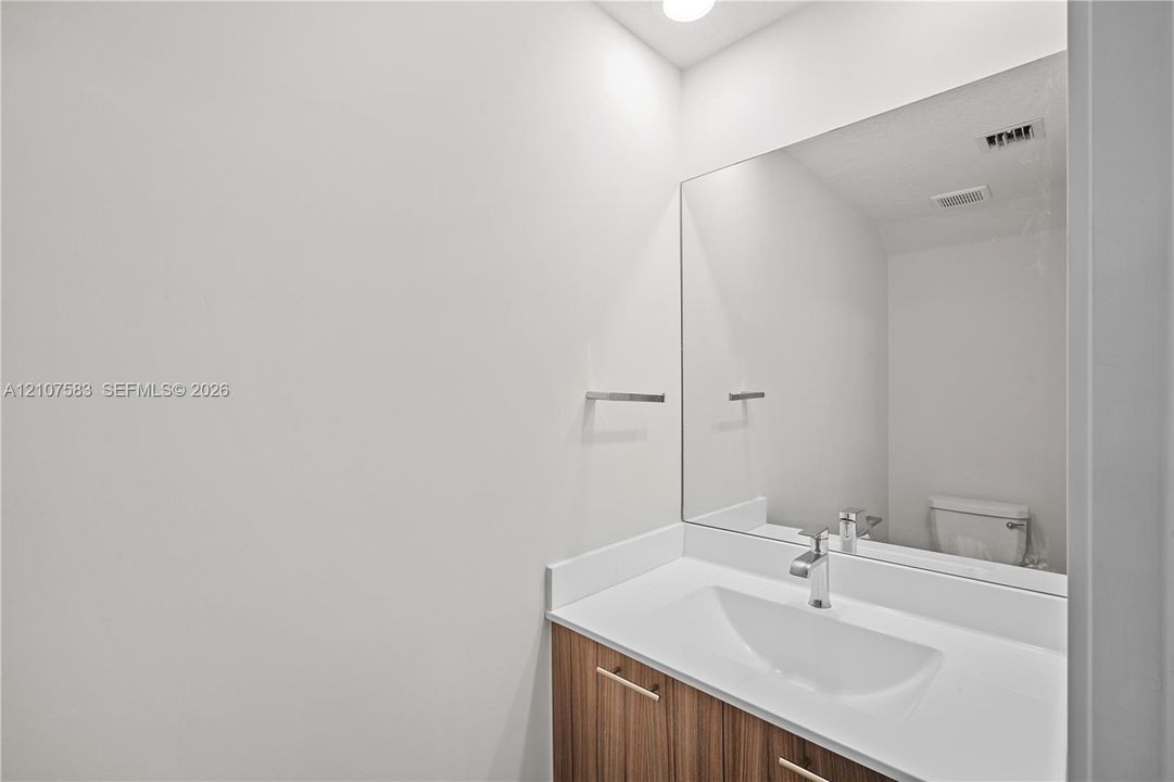 Vanity featuring a wood-finish cabinet, white solid-surface countertop with an integrated basin, wall-to-wall mirror, and a polished metal faucet