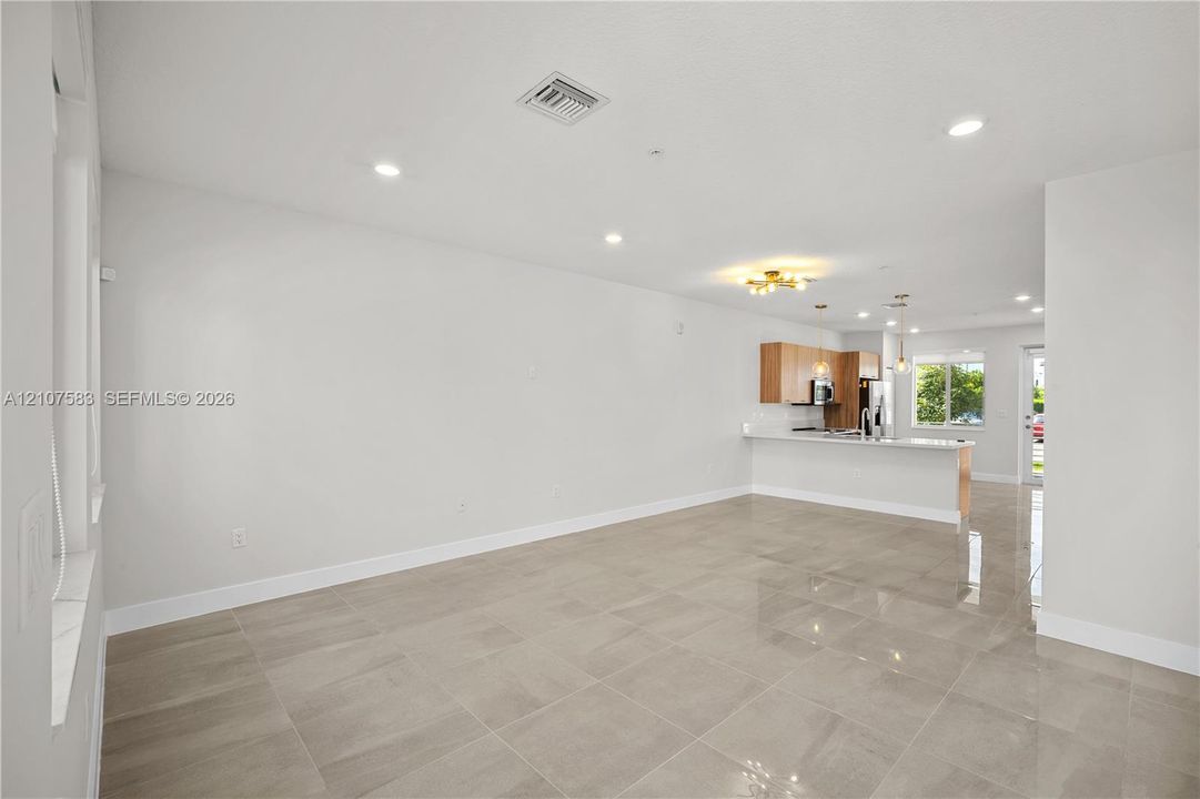 Open-concept interior featuring large-format tile flooring, recessed lighting, a kitchen island with a stone countertop, and light-toned cabinetry