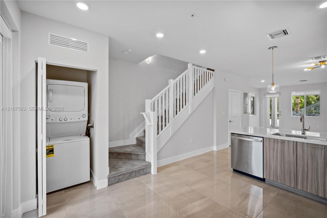 Neutral tile flooring, recessed lighting, white staircase with handrail, built-in laundry closet, and cabinetry with integrated stainless steel dishwasher