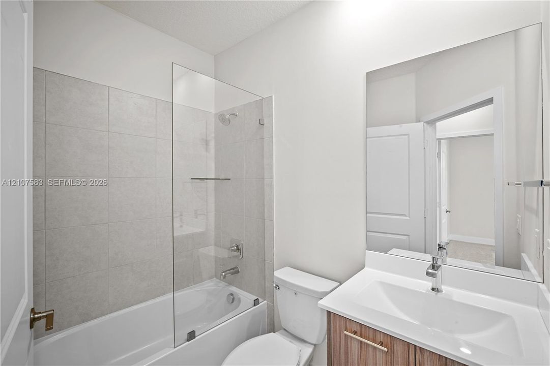 Bathroom featuring a tub-shower combination with floor-to-ceiling tile surround, a frameless glass panel, a wood-finish vanity with a rectangular integrated sink, and a large-format vanity mirror