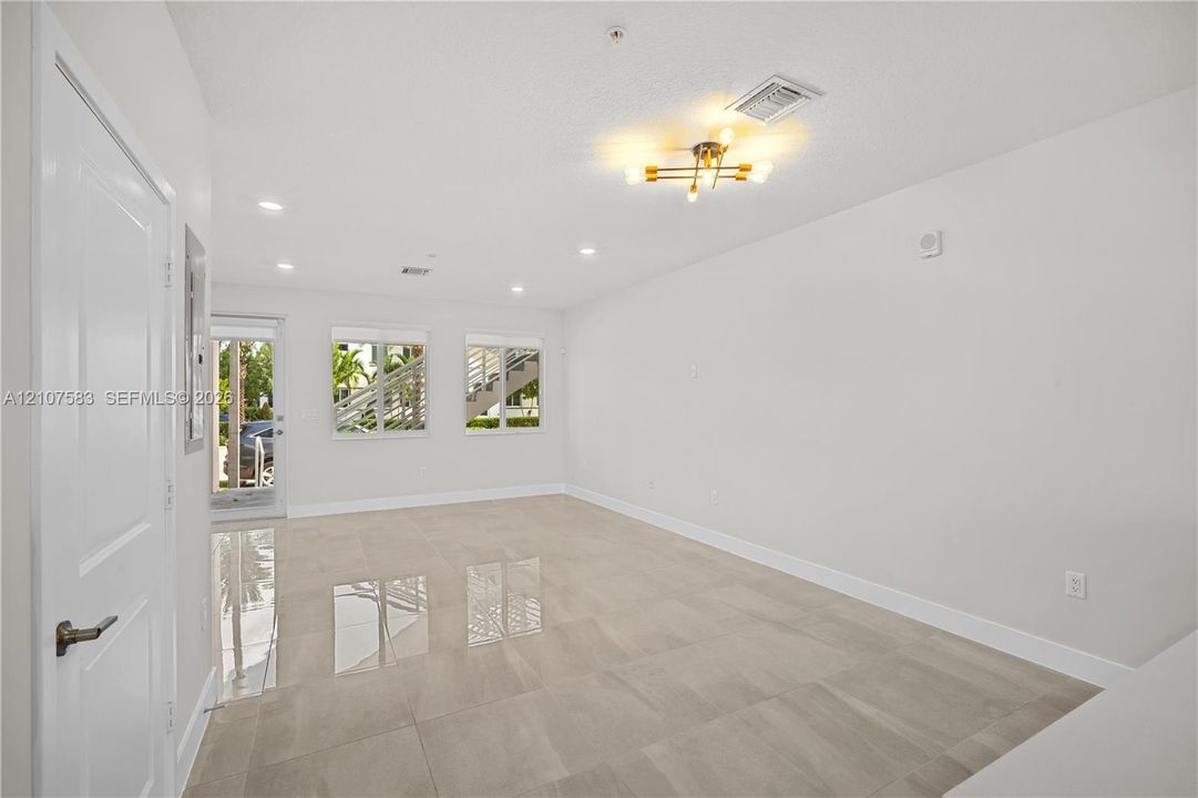 Open-concept interior featuring large-format tile flooring, recessed lighting, a modern multi-bulb ceiling fixture, and dual windows with exterior access via a glass-panel door