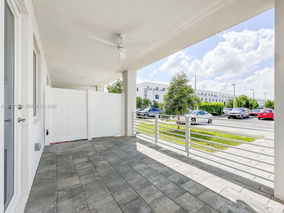 Covered outdoor patio featuring large-format tile flooring, a white vinyl privacy screen, and a ceiling-mounted fan