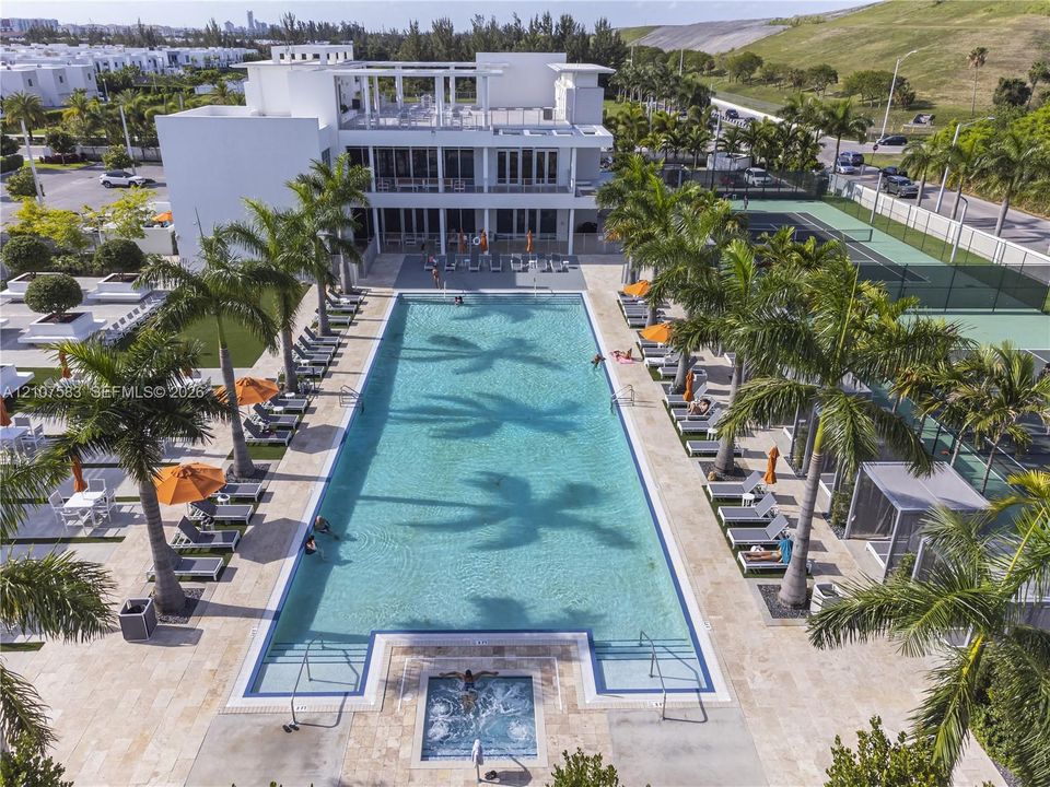 Rectangular swimming pool with integrated spa, stone-paver deck, professional-grade tennis court, and perimeter landscaping with palm trees