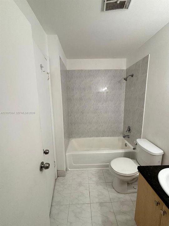 Full bathroom featuring a tub-shower combination with floor-to-ceiling tile surround, light-toned cabinetry, dark stone-finish countertop, and neutral tile flooring