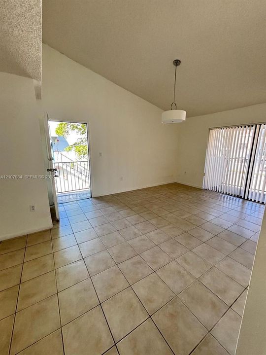 Vaulted ceiling, neutral tile flooring, drum-style pendant lighting, and sliding glass doors with vertical blinds