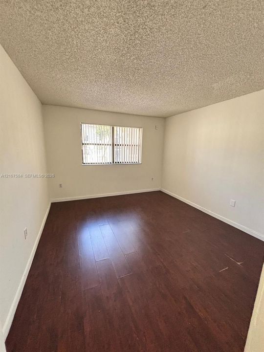 Interior room featuring dark wood-finish flooring, neutral wall coloring, and vertical window blinds