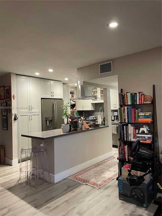 Kitchen featuring white shaker-style cabinetry, stainless steel appliances, a peninsula with a stone-surface countertop, and wood-finish flooring