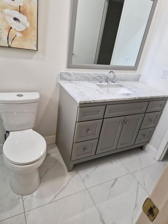 Bathroom featuring a gray vanity with stone-top surfacing, undermount sink, framed mirror, and large-format tile flooring