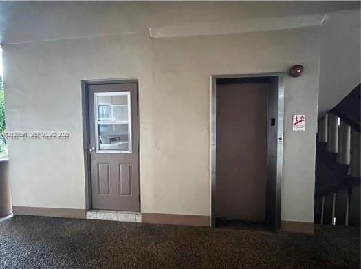 Single-panel entry door with a rectangular window insert, paired with a stainless steel elevator entrance