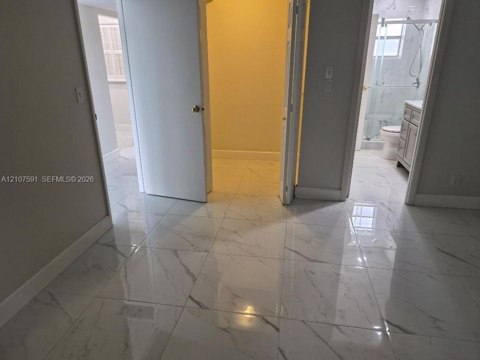 Large-format porcelain tile flooring with veining, walk-in closet with interior lighting, and bathroom featuring a vanity with cabinet storage and a glass-enclosed shower